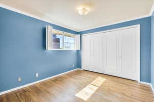 Unfurnished bedroom featuring ornamental molding, baseboards, wood finished floors, and a closet