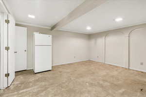 Basement with freestanding refrigerator, crown molding, and baseboards