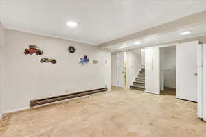 Finished basement featuring a baseboard heating unit, stairway, crown molding, and freestanding refrigerator
