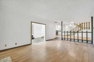 Unfurnished living room featuring stairway, wood finished floors, baseboards, and a textured ceiling