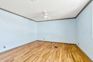 Empty room with crown molding, wood finished floors, baseboards, and a ceiling fan