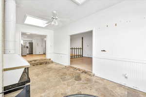 Empty room with a skylight, stone floors, a ceiling fan, and a wainscoted wall