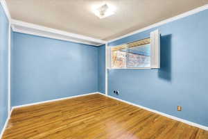Unfurnished room featuring ornamental molding, wood finished floors, baseboards, and a textured ceiling