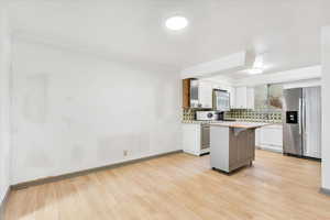 Kitchen with white appliances, light wood-type flooring, backsplash, light countertops, and a breakfast bar