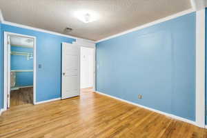 Unfurnished bedroom featuring ornamental molding, a textured ceiling, light wood-style floors, a walk in closet, and baseboards