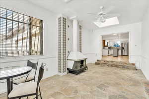 Dining area featuring stone flooring, a wood stove, ceiling fan, and a skylight
