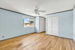 Unfurnished bedroom featuring ornamental molding, light wood-style flooring, multiple closets, baseboards, and a ceiling fan