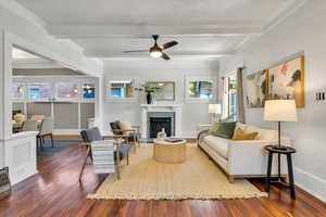 Living area with wood-type flooring, beam ceiling, a fireplace with flush hearth, baseboards, and ceiling fan