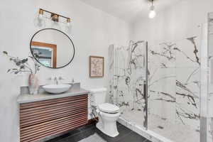 Full bath featuring vanity, a marble finish shower, and toilet