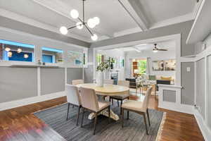 Dining area featuring wood-type flooring, beam ceiling, a fireplace, a chandelier, and ceiling fan