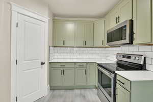 Kitchen featuring green cabinetry, appliances with stainless steel finishes, light countertops, and backsplash