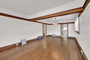 Unfurnished living room featuring dark wood finished floors, baseboards, and a chandelier