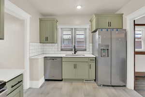 Kitchen featuring green cabinets, stainless steel appliances, a sink, light countertops, and recessed lighting