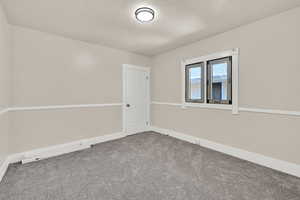 Empty room with carpet floors, a textured ceiling, and baseboards