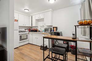 Kitchen with white appliances, light wood-style flooring, a sink, white cabinetry, and light countertops