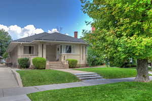 Bungalow featuring a front yard, a chimney, covered porch, and roof with shingles