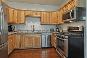Kitchen with stainless steel appliances, light stone counters, and dark wood finished floors