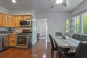 Kitchen featuring stainless steel appliances, light stone counters, dark wood-type flooring, ceiling fan, and brown cabinetry