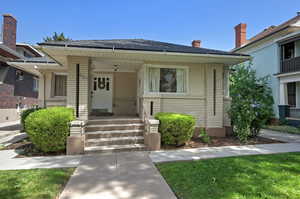 Property entrance with brick siding, a porch, roof with shingles, a chimney, and a lawn
