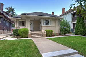 Bungalow-style house with a front lawn, a shingled roof, covered porch, and brick siding