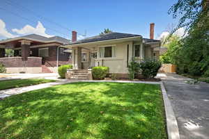 Bungalow-style home featuring covered porch, a chimney, a front yard, and brick siding
