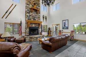 Living room with a high ceiling, a chandelier, a stone fireplace, and baseboards