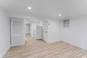 Basement featuring freestanding refrigerator, baseboards, light wood-style flooring, recessed lighting, and built in features