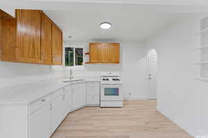 Kitchen with white range with gas stovetop, open shelves, a sink, and arched walkways