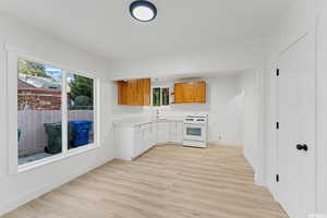 Kitchen featuring white range with gas cooktop, light countertops, light wood-style flooring, a sink, and baseboards