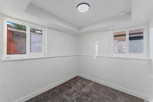 Empty room with a tray ceiling, dark colored carpet, baseboards, and a smoke detector