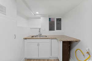 Kitchen with a sink, white cabinetry, baseboards, light wood finished floors, and light stone counters