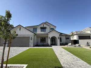 Modern farmhouse style home with stone siding, an attached garage, a front lawn, and board and batten siding