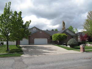 View of front facade with an attached garage, concrete driveway, brick siding, and a front yard