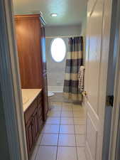 Bathroom featuring toilet, vanity, shower / bathtub combination with curtain, a textured ceiling, and tile patterned flooring