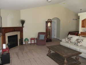 Carpeted living area with vaulted ceiling, a high end fireplace, arched walkways, and baseboards
