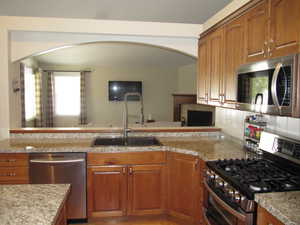 Kitchen featuring stainless steel appliances, a sink, arched walkways, and brown cabinetry