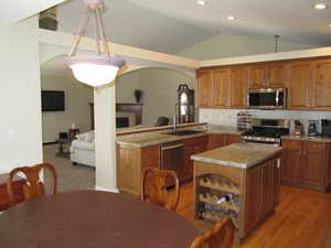 Kitchen featuring appliances with stainless steel finishes, light stone counters, vaulted ceiling, brown cabinets, and backsplash