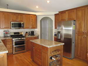 Kitchen with stainless steel appliances, light wood-style flooring, arched walkways, decorative backsplash, and recessed lighting