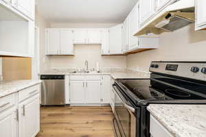 Kitchen with stainless steel appliances, a sink, under cabinet range hood, light wood-type flooring, and white cabinets
