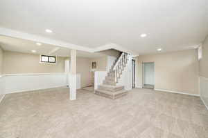 Below grade area with carpet flooring, recessed lighting, stairs, and a wainscoted wall