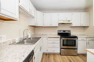 Kitchen with under cabinet range hood, stainless steel electric range, a sink, and white cabinetry