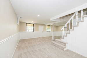Basement with a wainscoted wall, stairs, carpet flooring, and recessed lighting