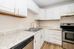 Kitchen featuring stainless steel appliances, under cabinet range hood, a sink, white cabinetry, and light countertops