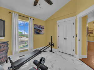 Workout area with vaulted ceiling, ceiling fan, light marble finish flooring, and baseboards