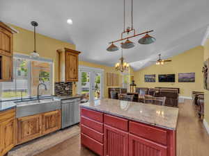 Kitchen featuring stainless steel dishwasher, a sink, a ceiling fan, vaulted ceiling, and decorative light fixtures