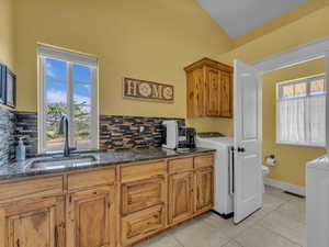 Kitchen with washer / clothes dryer, a sink, backsplash, and light tile patterned floors
