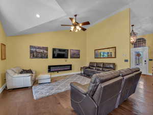 Living area with baseboards, dark wood-style floors, a glass covered fireplace, a ceiling fan, and a chandelier