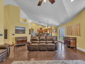 Living room with ceiling fan, a chandelier, wood finished floors, baseboards, and high vaulted ceiling