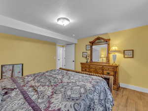Bedroom featuring wood finished porcelain tile floors, baseboards, and a textured ceiling