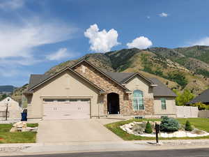 View of front of home featuring stucco siding, driveway, an attached garage, stone siding, and a mountain view